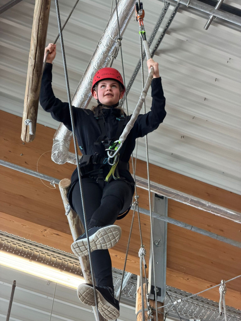 Person klettert im Indoor-Kletterpark mit Sicherheitsausrüstung