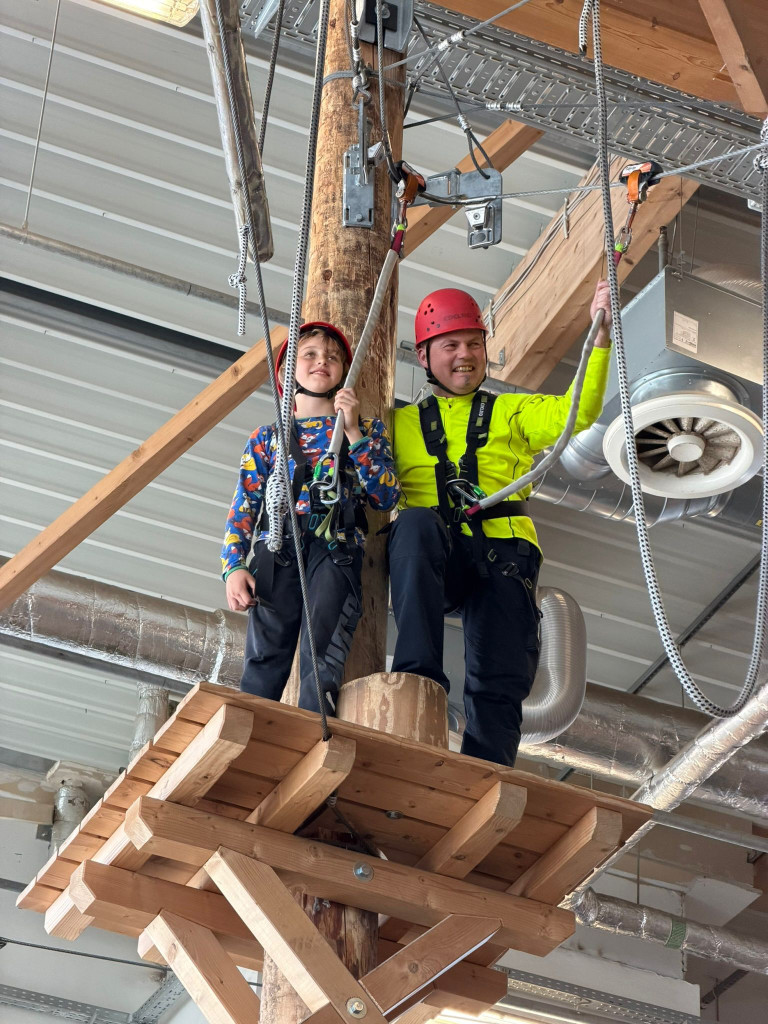 Zwei Personen mit Kletterausrüstung im Indoor-Kletterpark auf einer Holzplattform