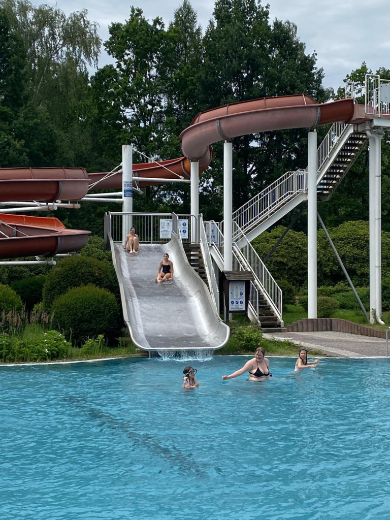 Wasserrutsche im Freibad – Sommerlicher Badespaß für Kinder und Erwachsene Kinder und Erwachsene rutschen im Freibad auf einer großen Wasserrutsche ins Schwimmbecken
