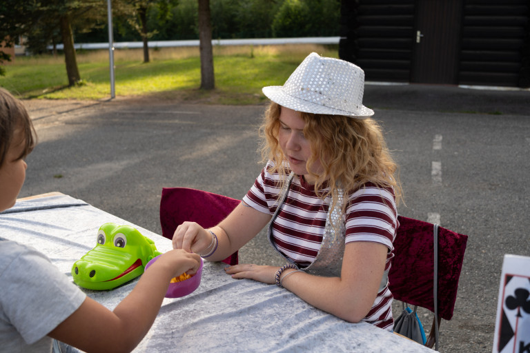 Sommerfest Seifhennersdorf: Junge Frau mit Paillettenhut und Kind am Tisch mit Spielzeug-Krokodil Junge Frau mit Paillettenhut beim Sommerfest in Seifhennersdorf am Tisch, Kind greift in eine Schüssel, Spielzeug-Krokodil auf dem Tisch