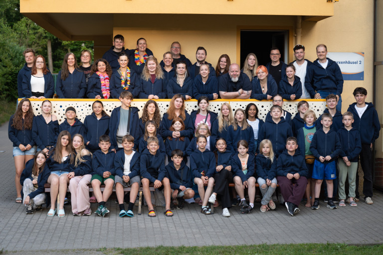 Gruppenbild Ferienfreizeitlager Seifhennersdorf 2023 – Jugendliche und Betreuer gemeinsam Gruppenfoto beim Ferienfreizeitlager in Seifhennersdorf, Jugendliche und Betreuer vor gelbem Gebäude, Sommer 2023