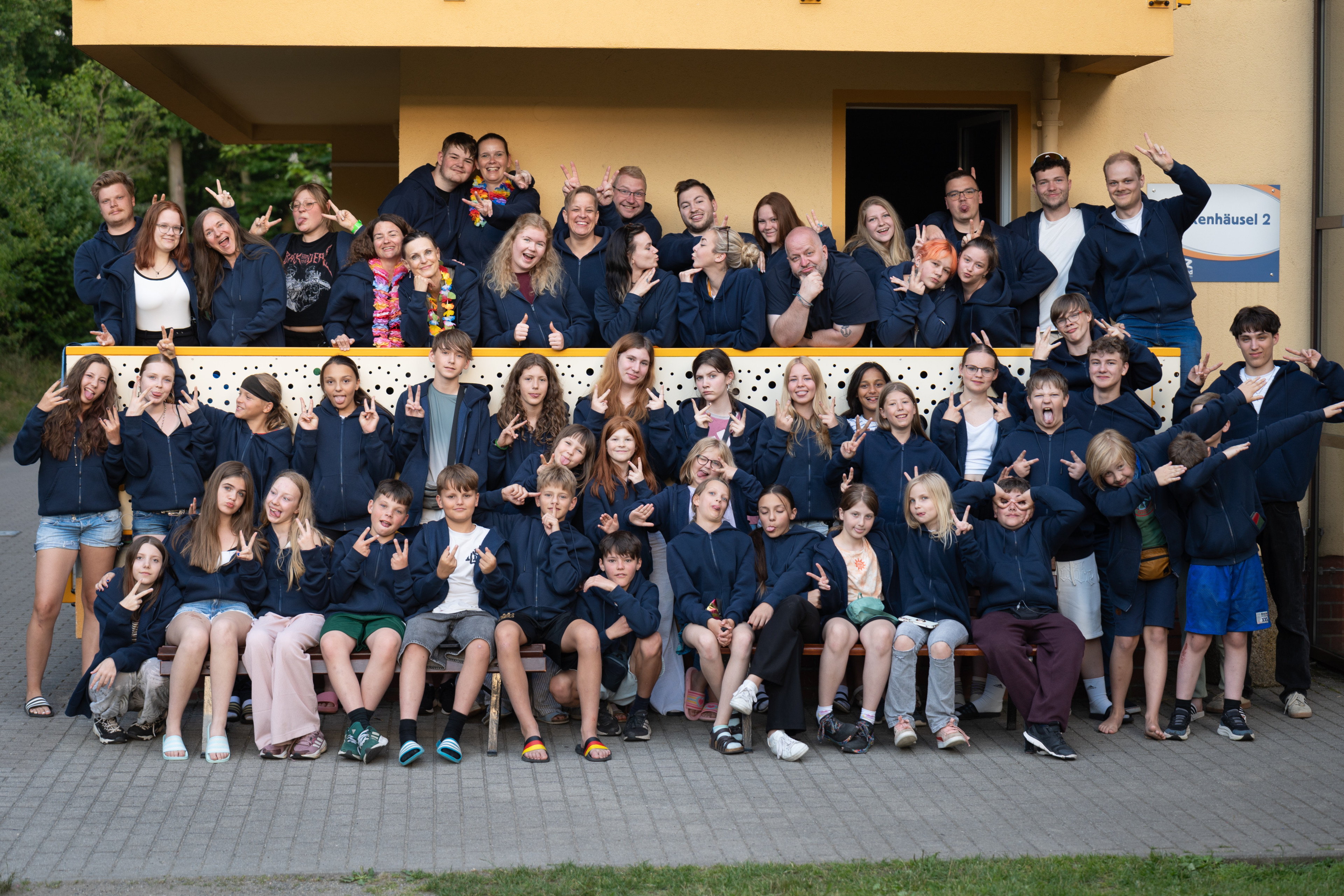 Gruppenfoto beim Ferienfreizeitlager FFZ26 in Seifhennersdorf, lachende Kinder und Betreuer vor gelbem Gebäude