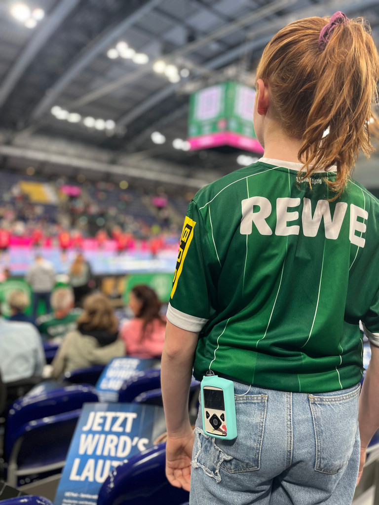 Handballspiel im Oktober mit grnem REWE-Trikot und pinken Akzenten in der Halle Handballspiel im Oktober mit Fokus auf eine Zuschauerin im grnen REWE-Trikot, pinke Elemente im Hintergrund
