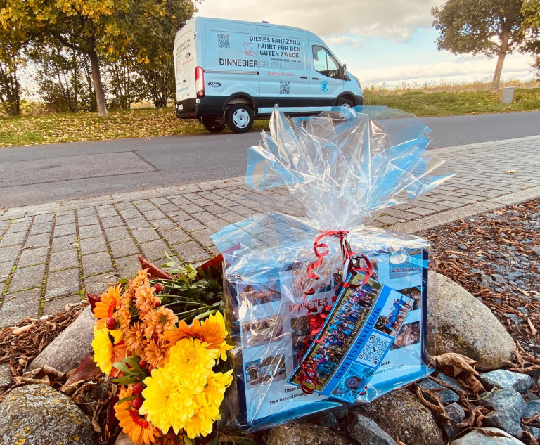Geschenk und Blumenstrauß vor Dinnebier Gruppe Transporter für wohltätigen Zweck am 19. Oktober 2026 Geschenkset mit Blumenstrauß und Präsentkorb vor einem Transporter der Dinnebier Gruppe für den guten Zweck