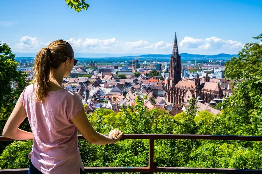 Aussicht auf Freiburg und das Freiburger Münster – Frau genießt den Ausblick Frau mit Sonnenbrille blickt auf die Altstadt von Freiburg mit dem Freiburger Münster im Hintergrund