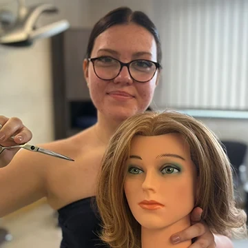 Jessica beim Haareschneiden an einem Übungskopf im Friseursalon