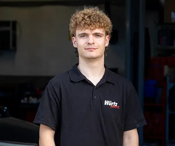 Darian Wözel vor einer Werkstatt, trägt ein schwarzes Würtz Autohaus Polo-Shirt