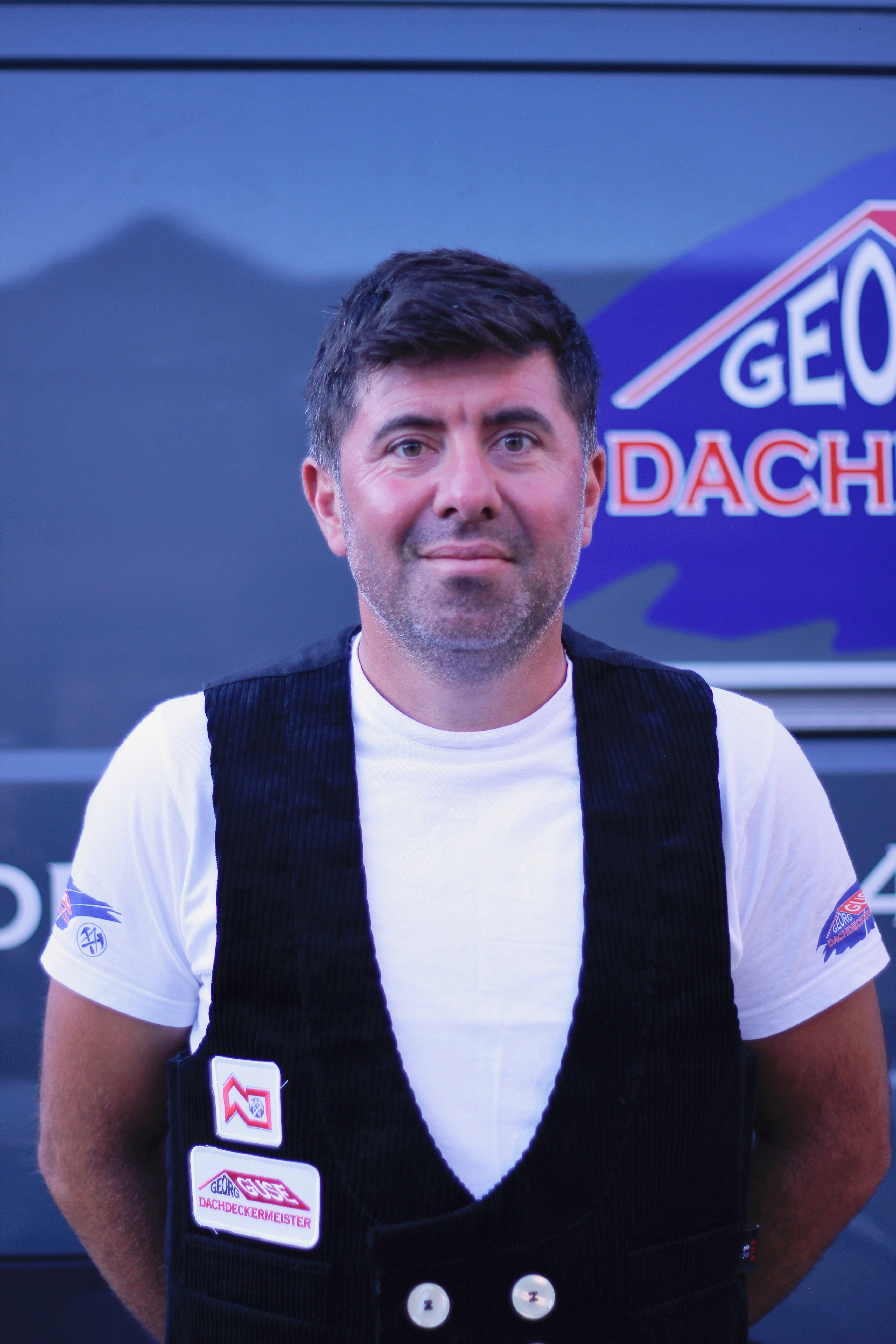 Fachgeselle Sabri Godce vor Firmenlogo GEO Dach