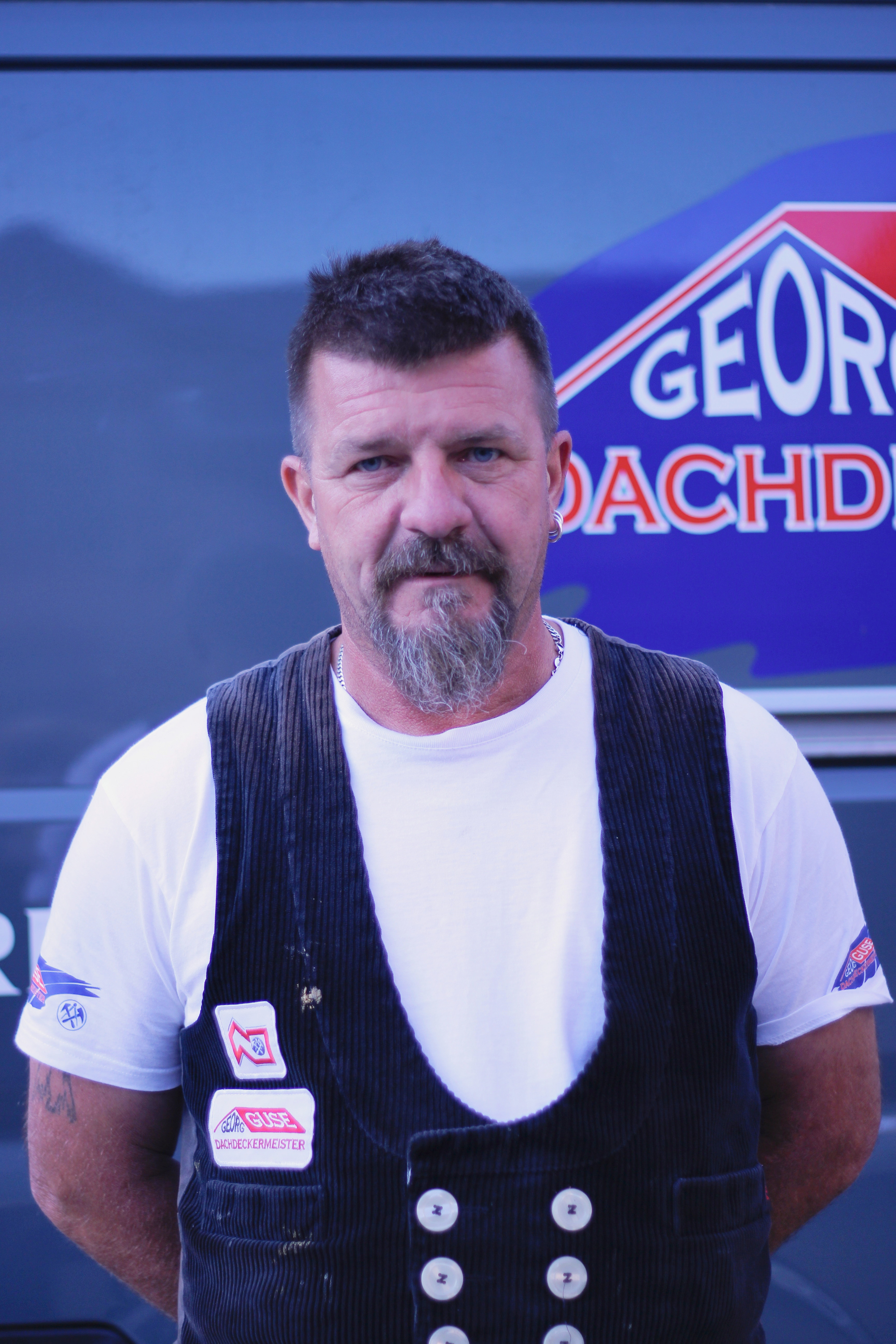 Fachgeselle Thorsten Heller vor Firmenlogo von Georg Dachdecker