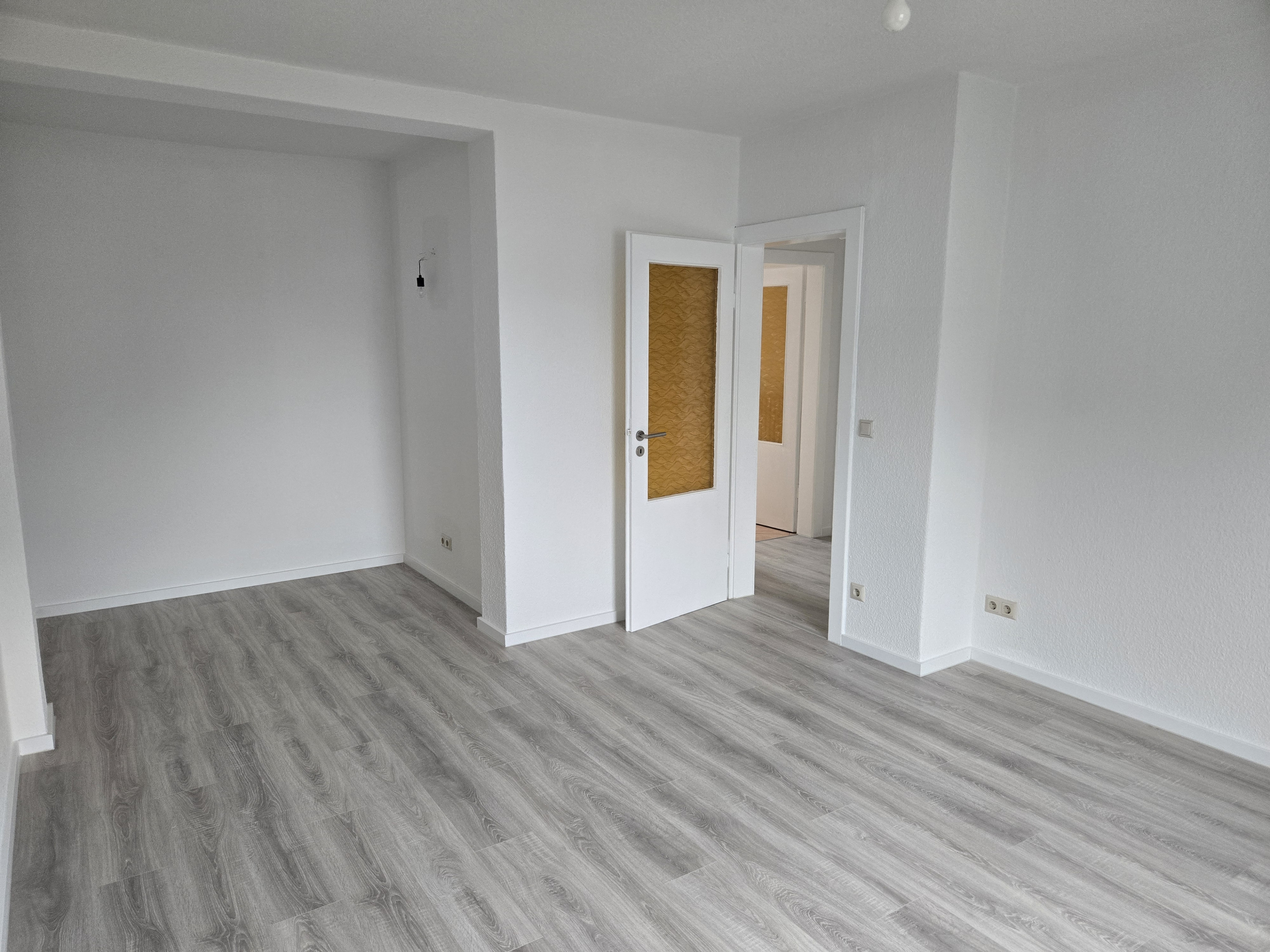 Leeres, frisch renoviertes Zimmer mit grauem Laminatboden und weißen Wänden, aufgenommen am 24.02.2026