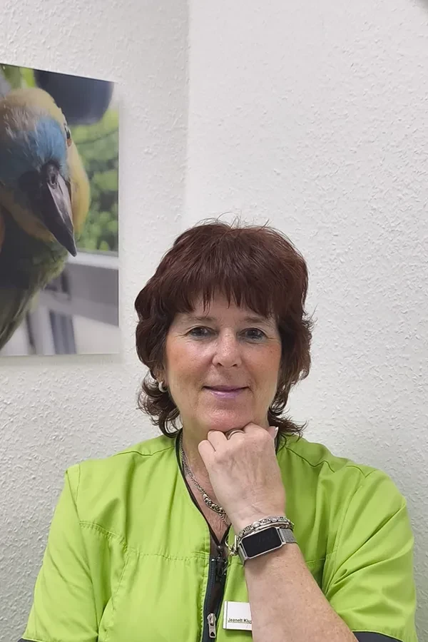 Frau Kluge in grüner Kleidung vor weißer Wand mit Papageienbild