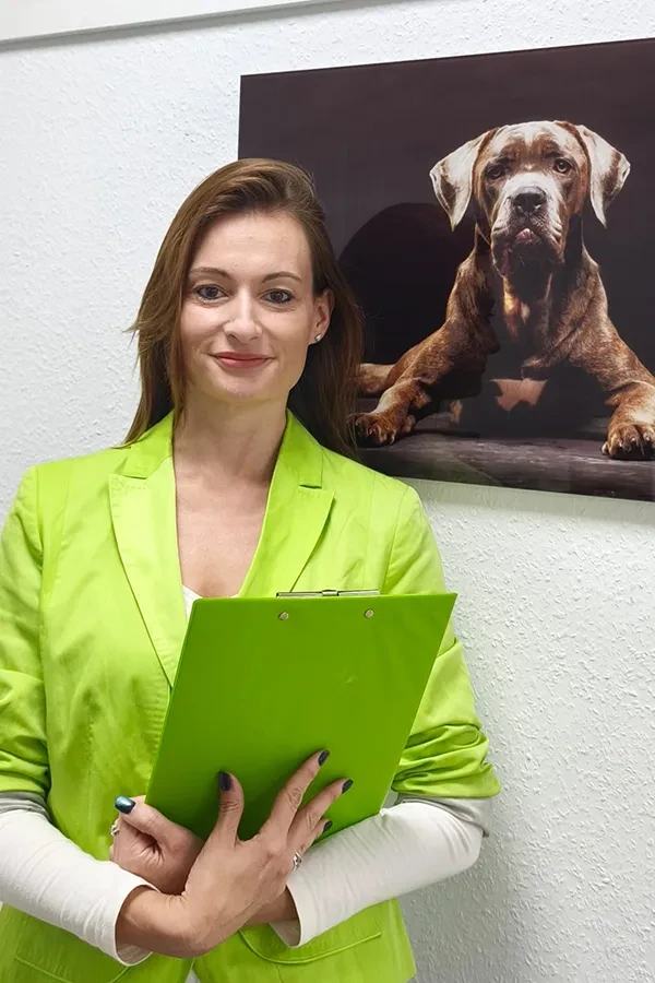 Frau Göbel mit grünem Blazer und Klemmbrett vor einem Hundebild
