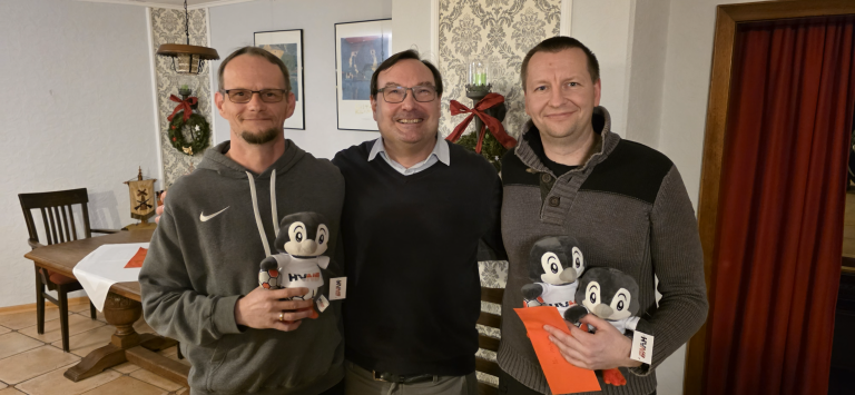 Drei Personen mit HVAM-Pinguin-Maskottchen und Weihnachtsdekoration im Hintergrund