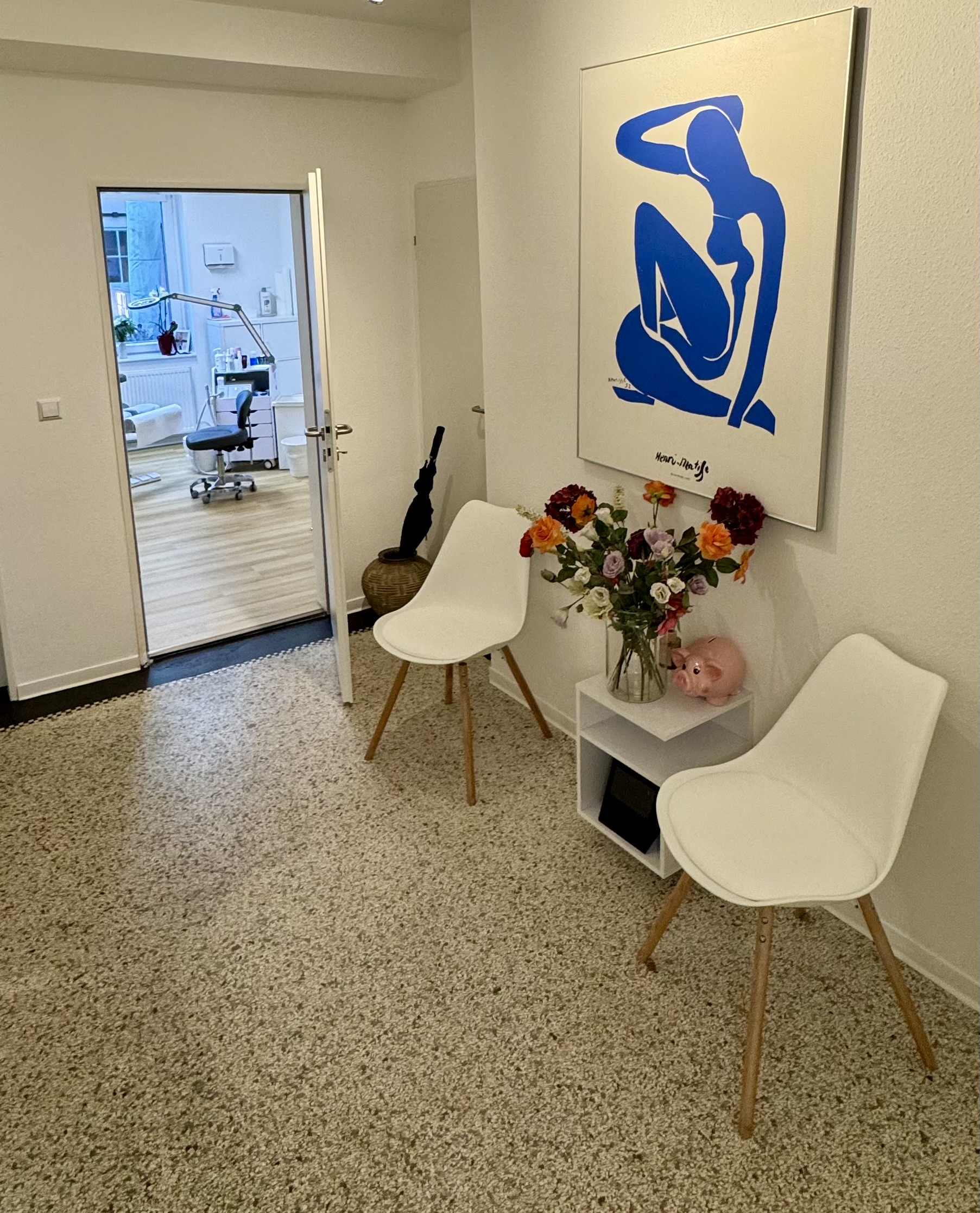 Wartezimmer einer Zahnarztpraxis mit weißen Stühlen, Blumenstrauß und moderner Wandkunst