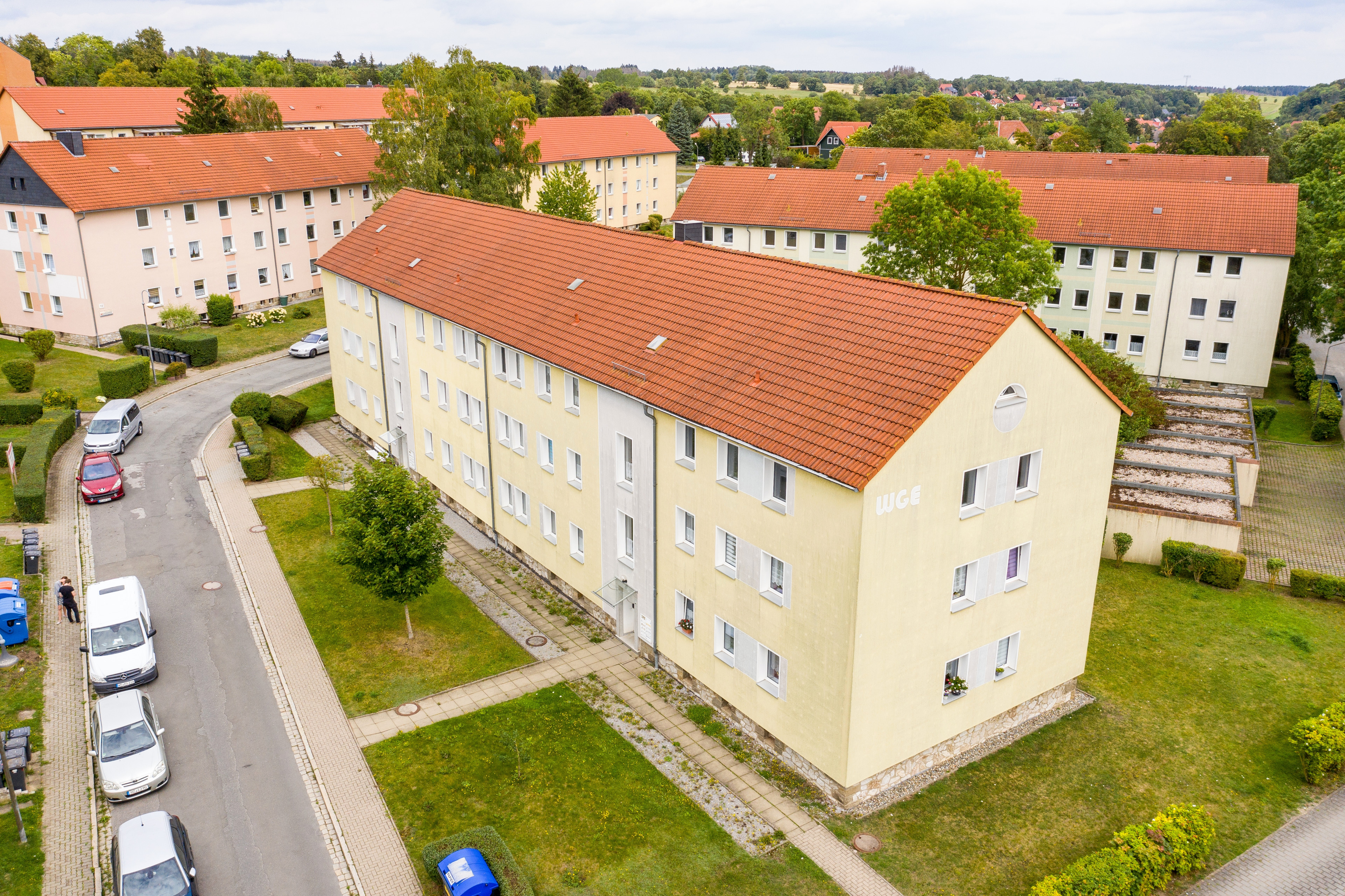 Luftaufnahme eines WGE Wohngebäudes mit gelber Fassade und rotem Dach in einer Wohnsiedlung