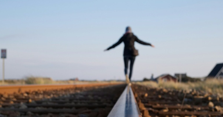 Person balanciert auf einem Gleis – Symbol für Gleichgewicht und Balance