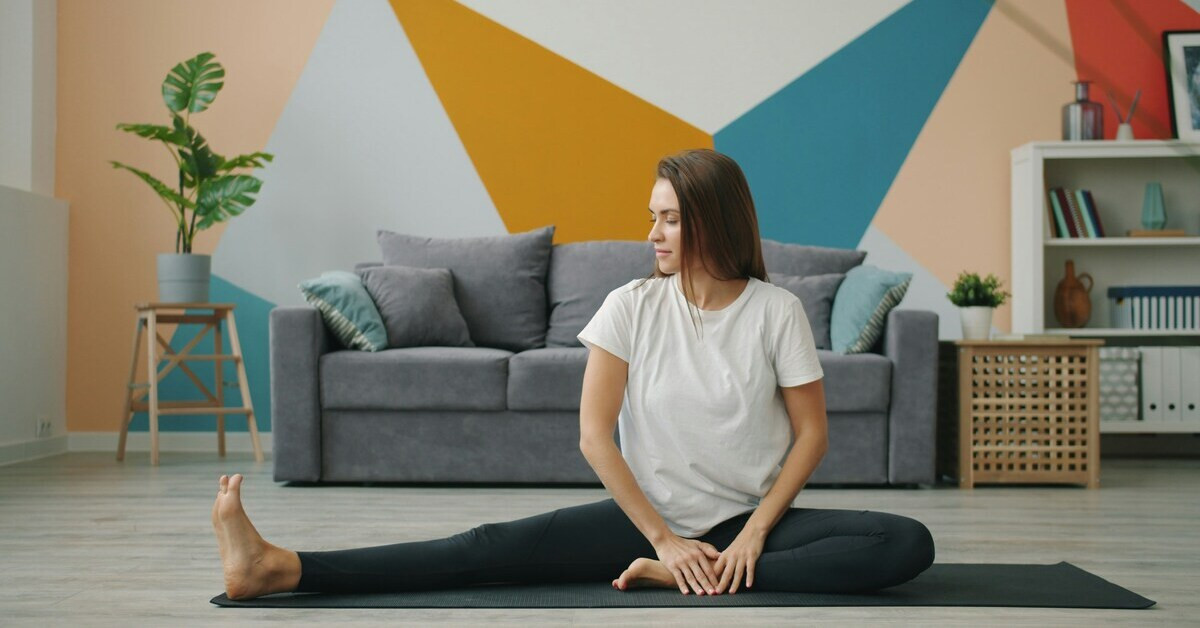 Frau sitzt auf einer Matte und macht Dehnübungen im Wohnzimmer