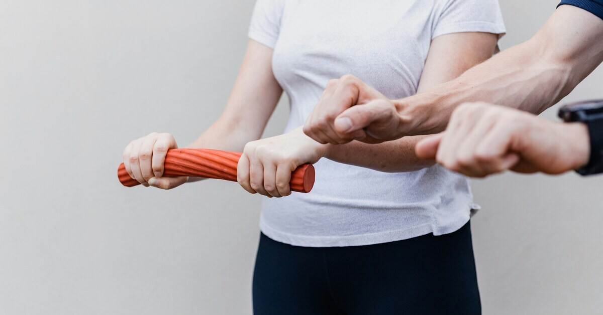 Krankengymnastik nach OP: Therapeut unterstützt Patientin bei Rehabilitationsübung mit Trainingsstab