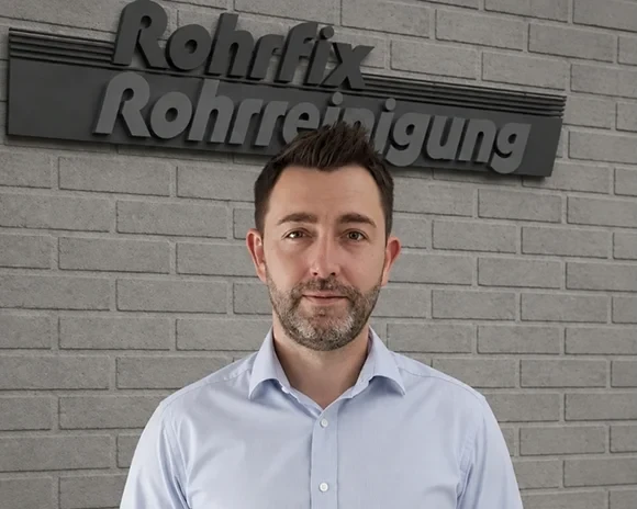 Steffen Uecker, Geschäftsführer von Rohrfix Rohrreinigung, vor Firmenlogo