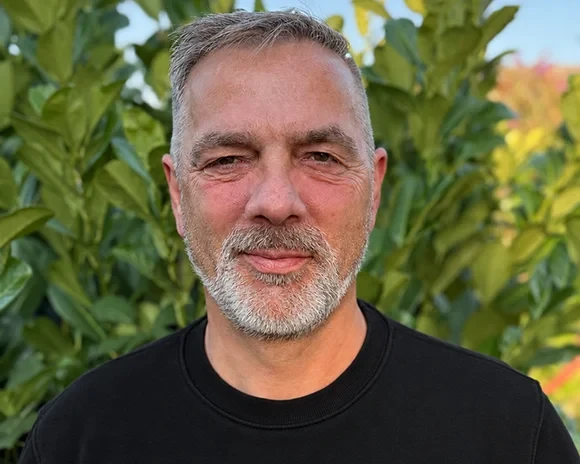 Portrait von Bodo Deichmann vor grünen Pflanzen