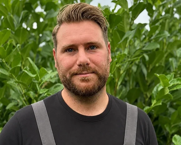 Porträt von Daniel Roloff vor grünen Pflanzen