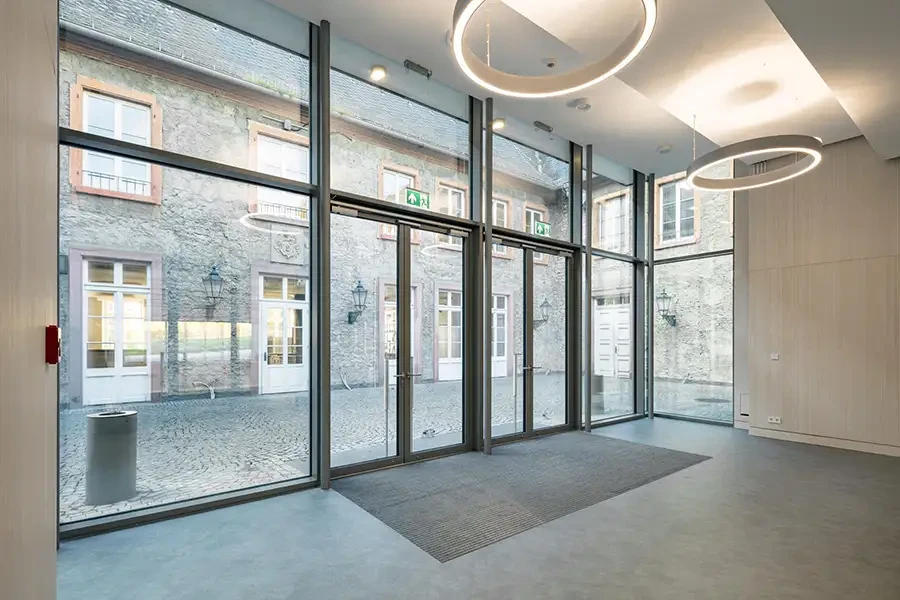 Moderne Glasfassade mit Blick auf historischen Innenhof, große Fensterfront und runde Deckenleuchten