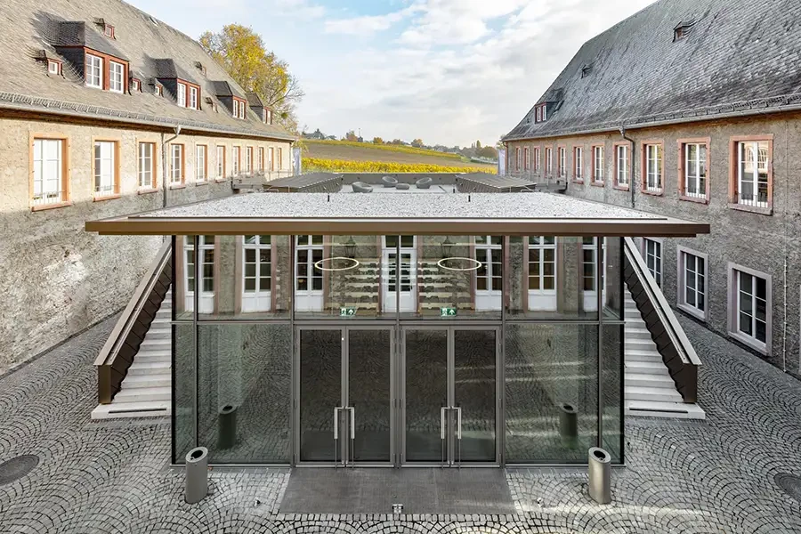 Modernes verglastes Eingangsgebäude zwischen historischen Gemäuern mit Blick auf Weinberge