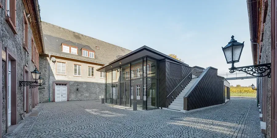 Modernes gläsernes Gebäude mit Außentreppe auf einem gepflasterten Innenhof