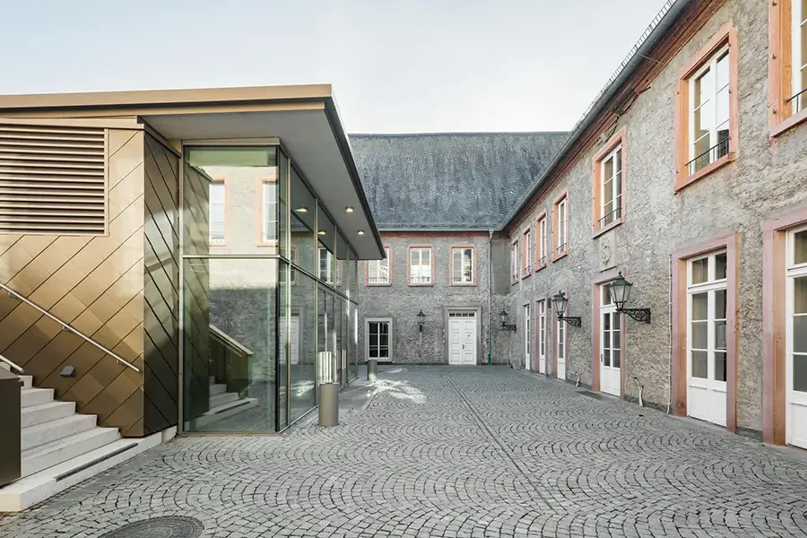 Moderner Glas-Anbau trifft auf historischen Innenhof mit Kopfsteinpflaster und klassischer Architektur