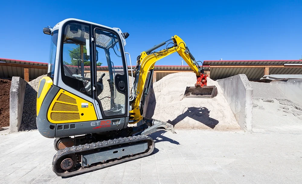 Bagger beim Bewegen von Schüttgütern auf einem Lagerplatz Bagger bewegt Schüttgüter auf einem Lagerplatz bei sonnigem Wetter
