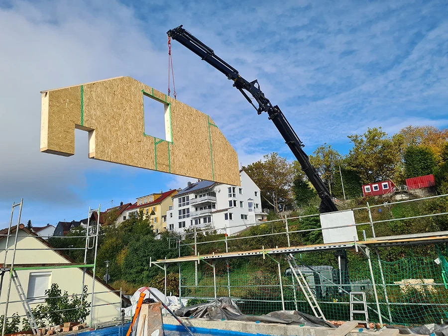Krandienst hebt Holzelement auf Baustelle vor Wohnhäusern