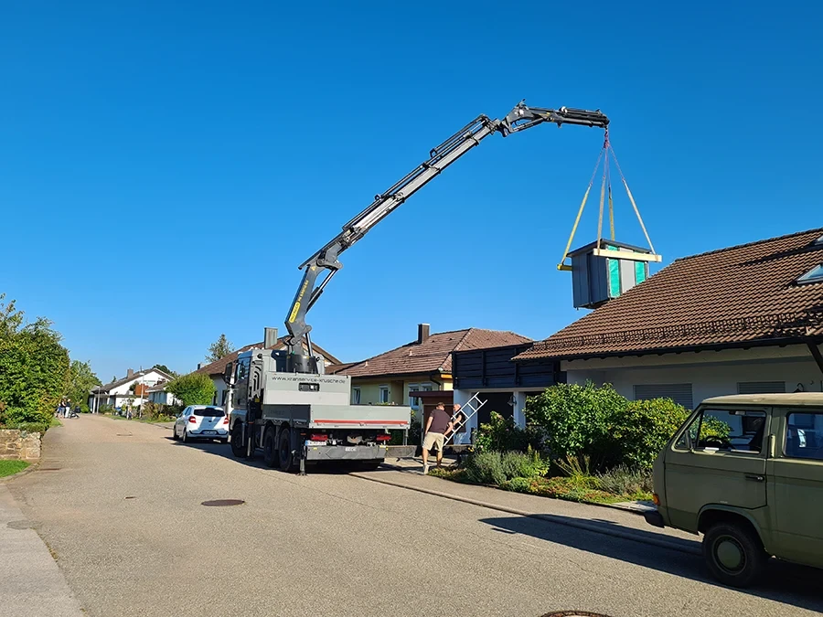 Krandienst hebt Modul mit LKW-Kran auf Hausdach in Wohngebiet