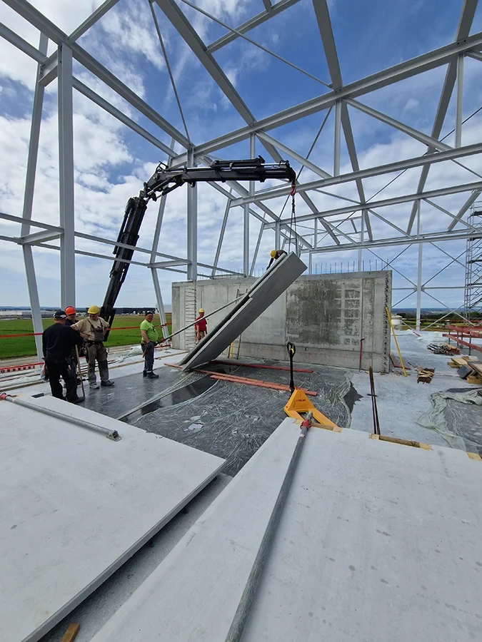 Krandienst hebt Betonplatte auf Baustelle mit mehreren Arbeitern