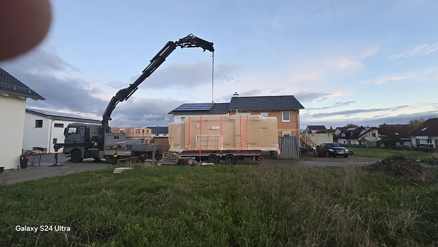 Krandienst beim Heben einer großen Kiste vor einem Neubauhaus