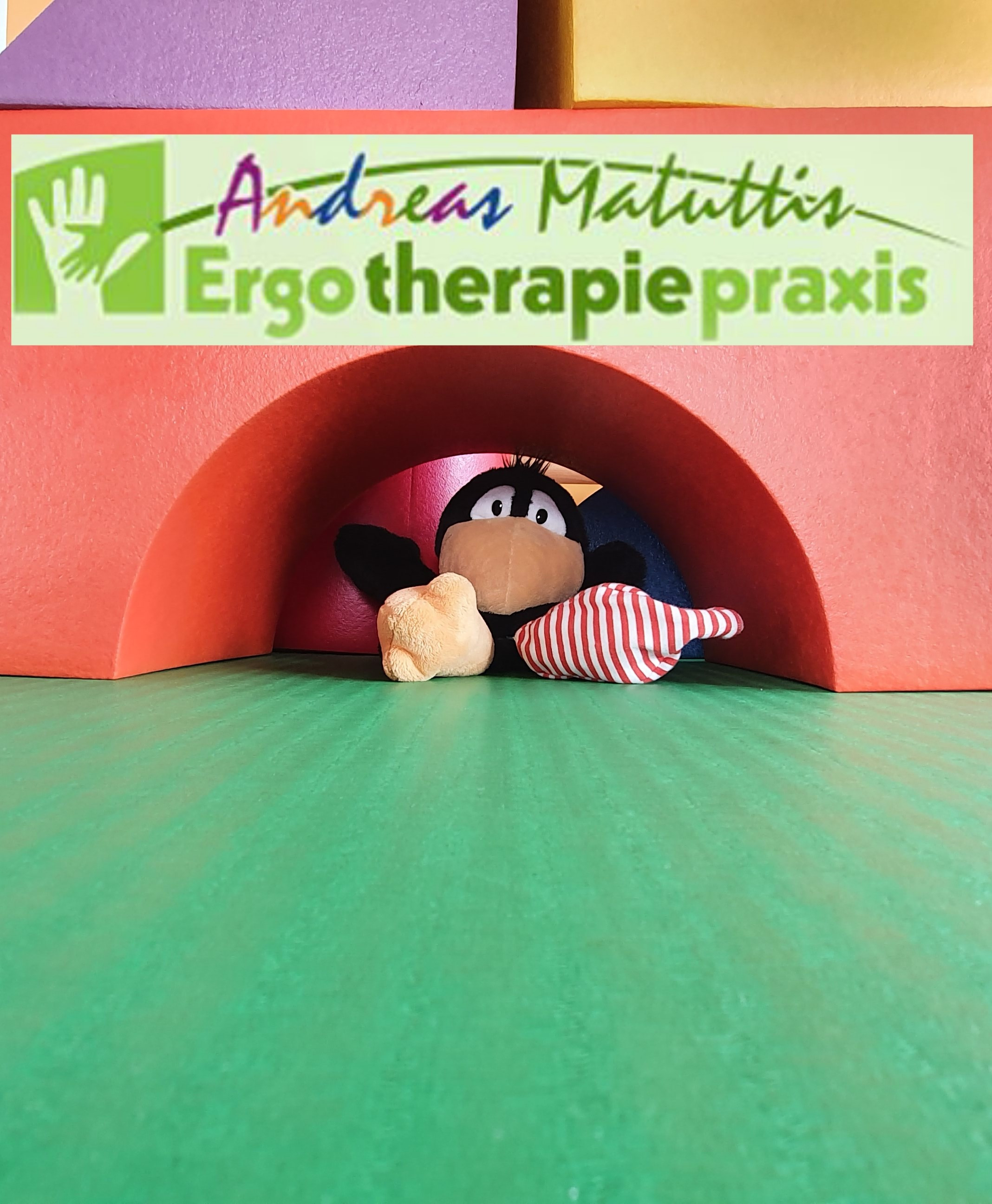 Rabe Socke in der Ergotherapiepraxis Andreas Matuttis unter einem roten Bogen mit grünem Boden