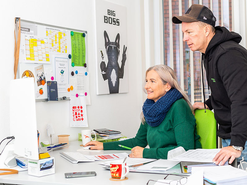 Zwei Personen arbeiten gemeinsam im modernen Büro von Kanal Kost, mit Unterlagen und Computer am Schreibtisch.