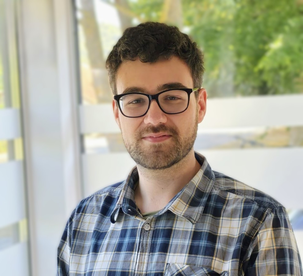 Porträt eines jungen Mannes mit Brille und kariertem Hemd vor einem Fenster, img-20260813-wa00053-002
