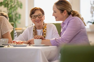 Zwei Frauen sitzen gemeinsam am Tisch und unterhalten sich bei Kaffee in gemütlicher Atmosphäre.