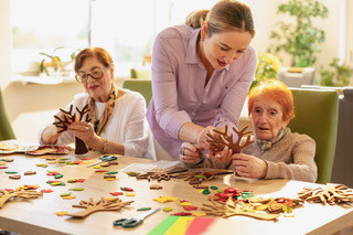 Bastelaktivität mit Senioren und Kindern an einem Tisch, herbstliche Dekorationen werden gemeinsam gestaltet