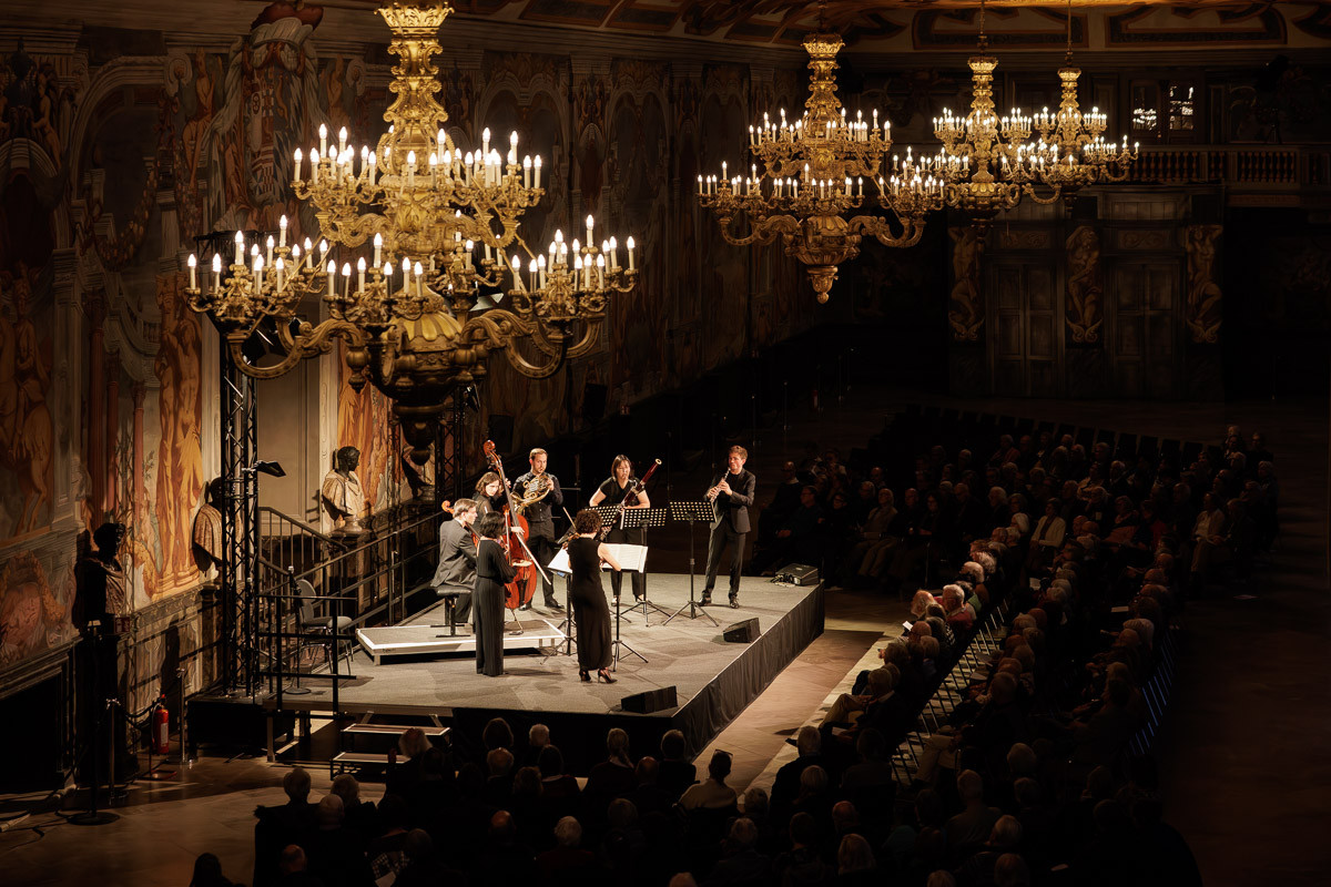 Konzert in prunkvollem Saal mit Kronleuchtern und klassischem Ensemble auf der Bühne, galerie-2