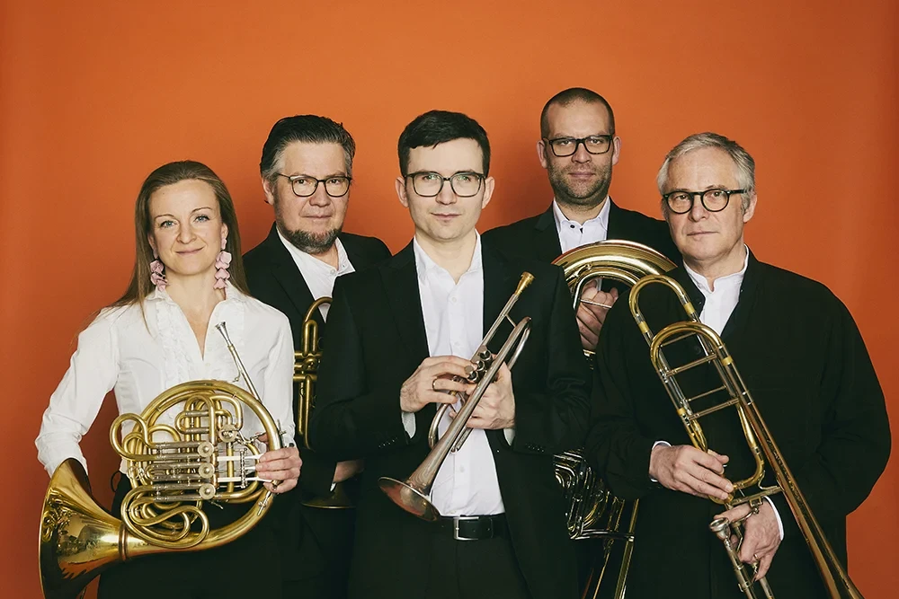 Stockholm Chamber Brass Ensemble mit fünf Musikern und ihren Blechblasinstrumenten vor orangem Hintergrund