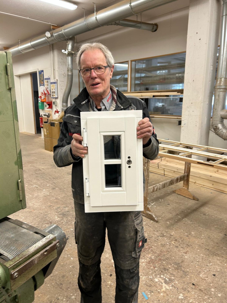 Handwerker hält ein weißes Miniaturmodell einer Haustür in einer Werkstatt