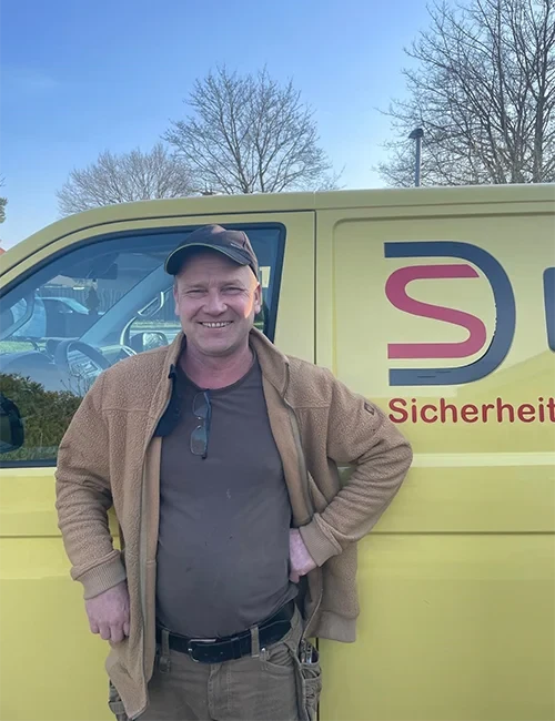 Portraitfoto von Tischler und Monteur Alex Masiutkin vor einem gelben Sicherheitsdienst-Fahrzeug