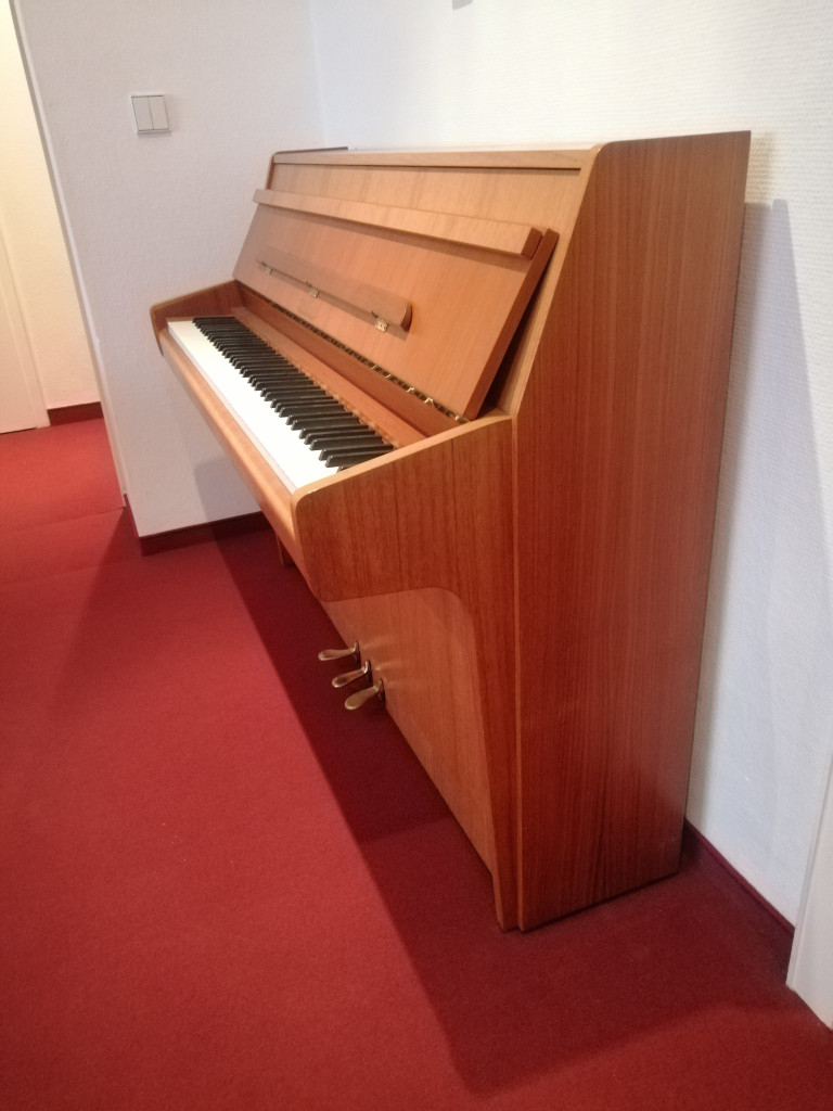 Modernes Klavier aus Holz auf rotem Teppich in einem Raum, Seitenansicht