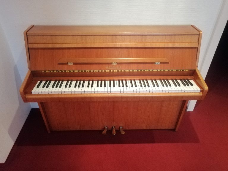 Schimmel Klavier aus Holz auf rotem Teppichboden