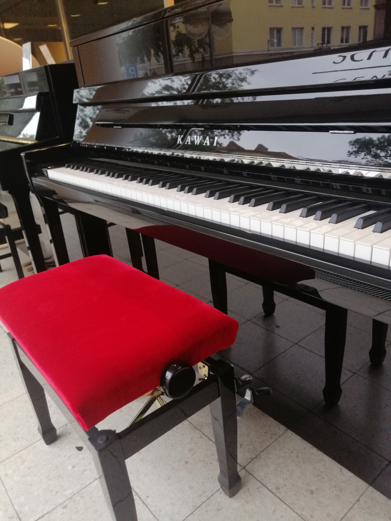 Kawai Klavier und roter Klavierhocker im Musikgeschäft Kawai Klavier mit rotem Klavierhocker in einem Musikgeschäft