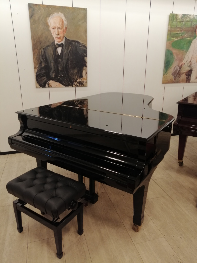 Schwarzer Flügel mit Hocker in einer Galerie mit Gemälden an der Wand