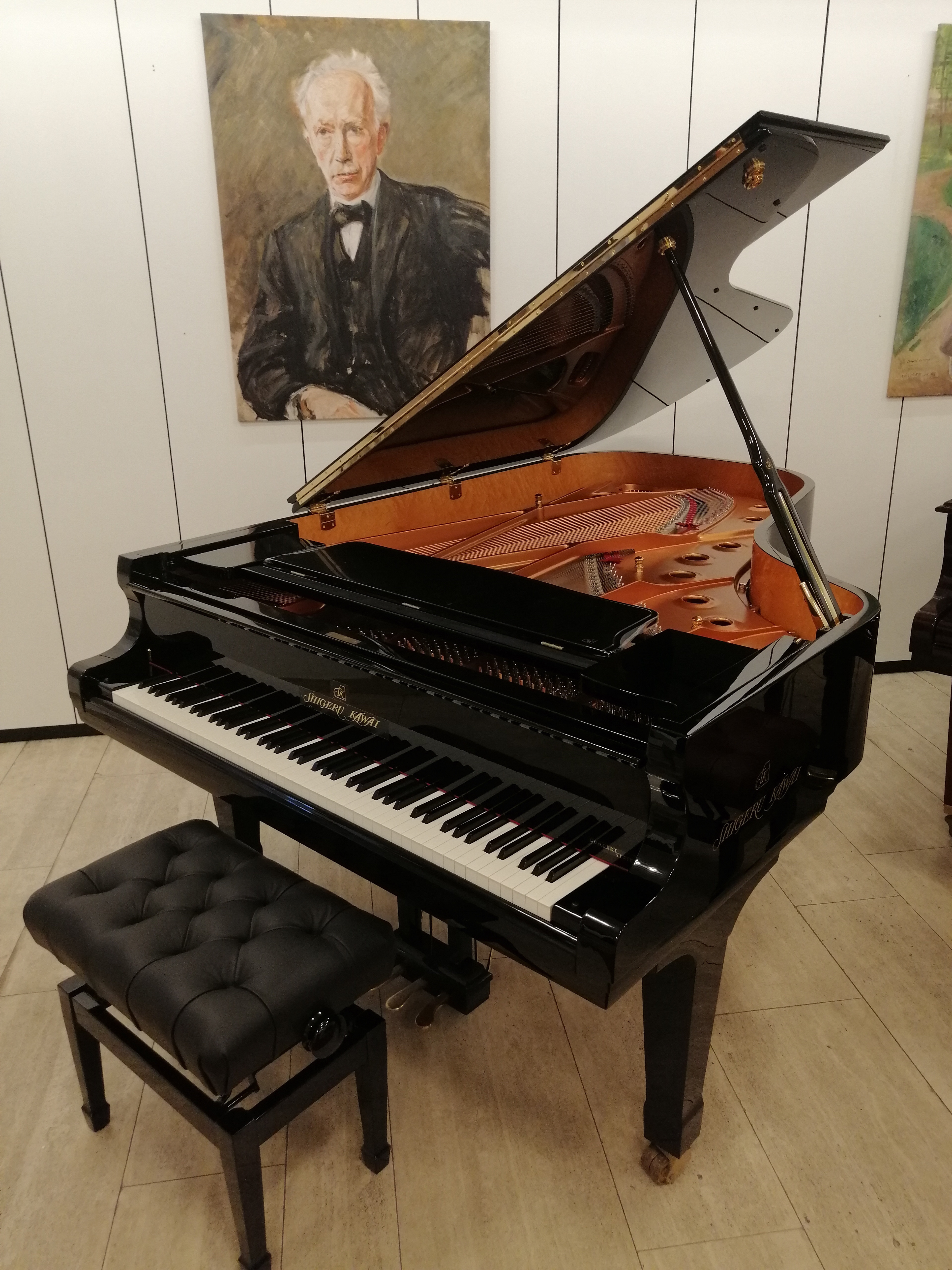 Flügel von Shigeru Kawai in einem Ausstellungsraum mit Klavierbank und Gemälde im Hintergrund