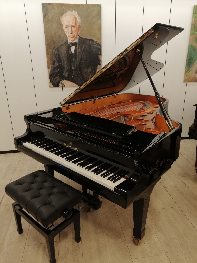 Flügel von Shigeru Kawai in einem Ausstellungsraum mit Klavierbank und Gemälde im Hintergrund