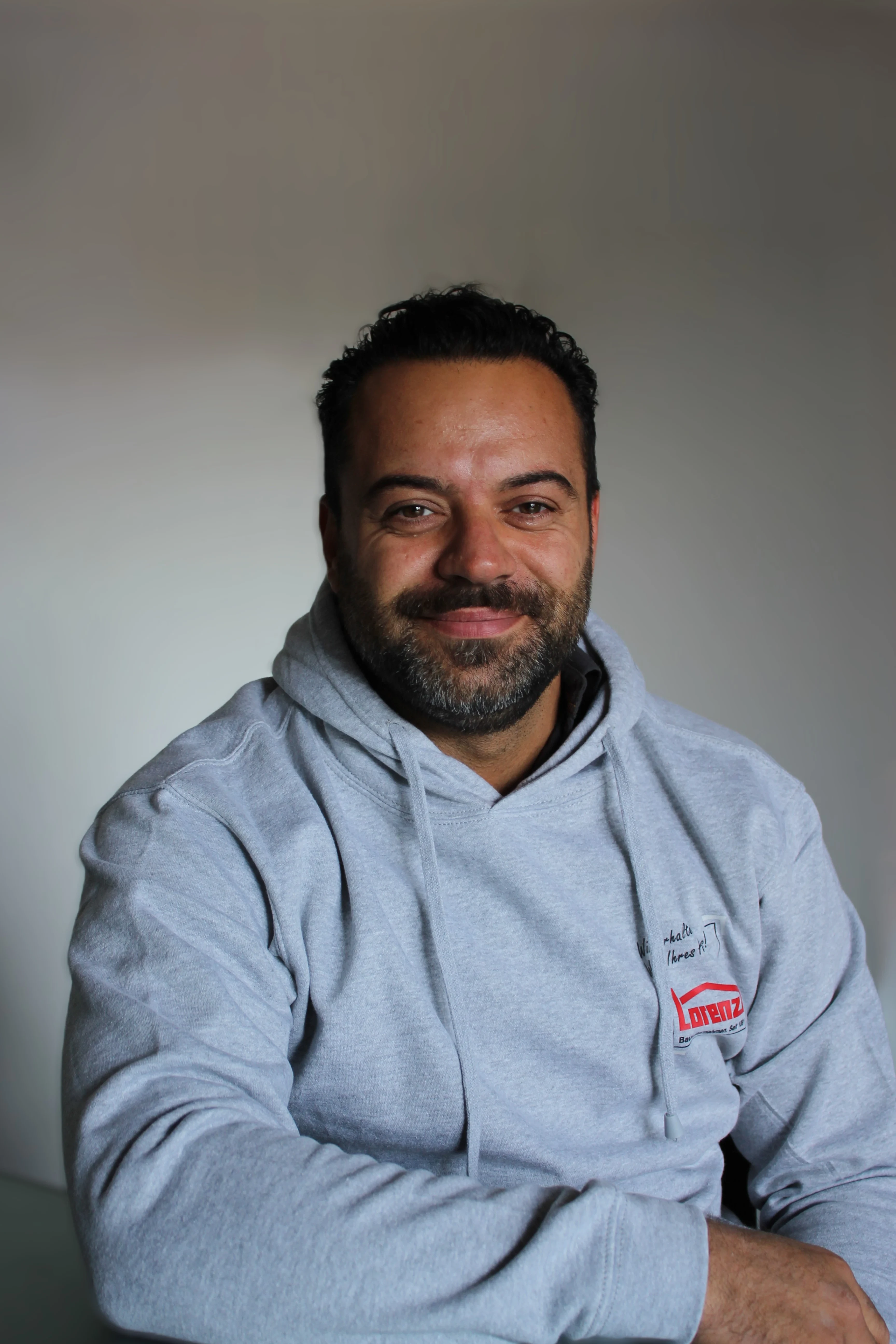 Kamrian Kinik mit grauem Lorenz-Hoodie vor neutralem Hintergrund